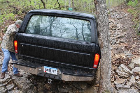 1979 Ford Bronco - A black 1979 Ford Bronco is seen from the rear, navigating a difficult rocky trail and getting close to a tree.