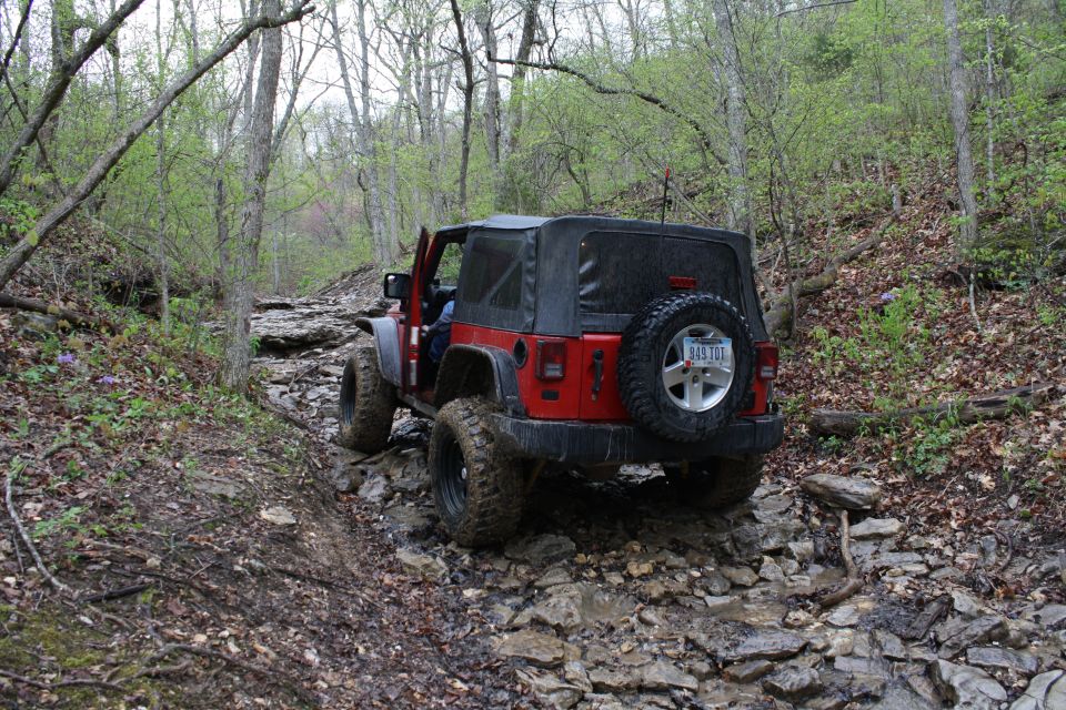 Red Jeep Wrangler driving over rocks on a wooded trail