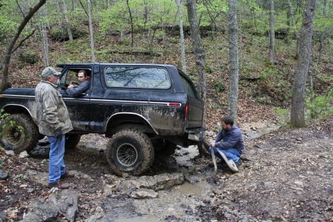 1979 Ford Bronco - A black 1979 Ford Bronco navigates a challenging muddy trail with assistance from onlookers.