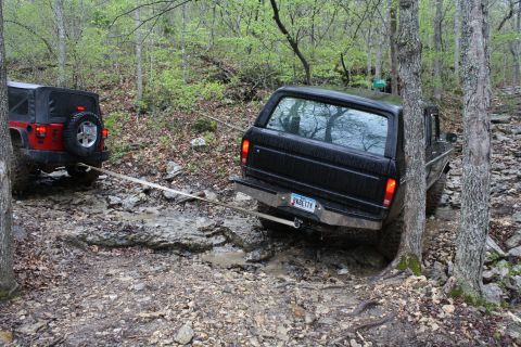 1979 Ford Bronco - Two off-road vehicles navigate a challenging, muddy path through a dense forest.