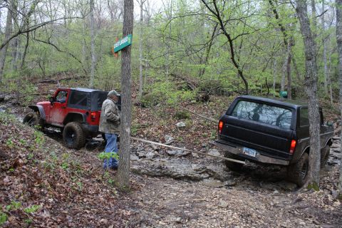 1979 Ford Bronco - A black 1979 Ford Bronco is being towed by a red Jeep while navigating a challenging, muddy off-road course.