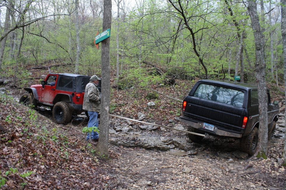 Black 1979 Ford Bronco rear view, being towed by a red Jeep on a muddy trail