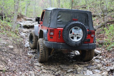 1979 Ford Bronco - A red Jeep Wrangler drives off-road on a challenging, rocky path.