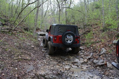 1979 Ford Bronco - A red Jeep Wrangler navigates a challenging, rocky off-road trail.