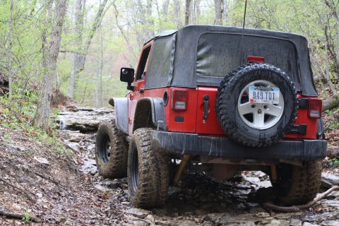 1979 Ford Bronco - Red Jeep Wrangler navigates a challenging rocky and muddy off-road trail.