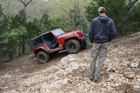 1979 Ford Bronco - A red Jeep Wrangler Rubicon navigates a challenging off-road trail while a man observes the ascent.