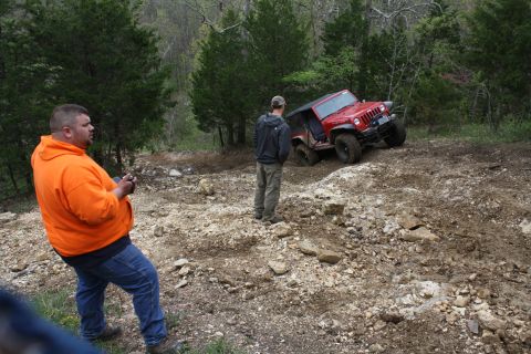 1979 Ford Bronco - A red Jeep Wrangler navigates a challenging off-road trail with spectators observing the action.