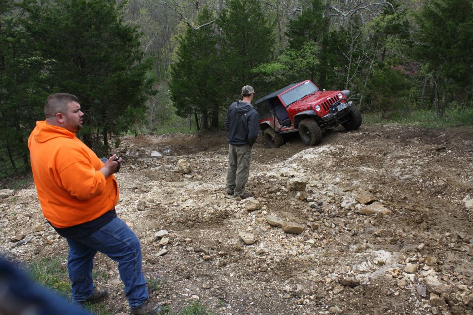 Red Jeep Wrangler climbing a dirt hill with two people watching