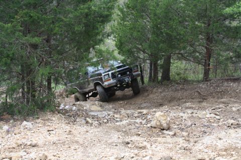 1979 Ford Bronco - A black 1978 Ford Bronco navigates a muddy, rocky incline in a wooded area.