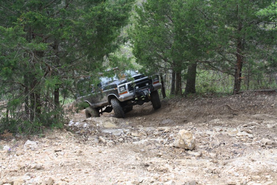Black 1978 Ford Bronco off-roading on a dirt hill with trees in the background