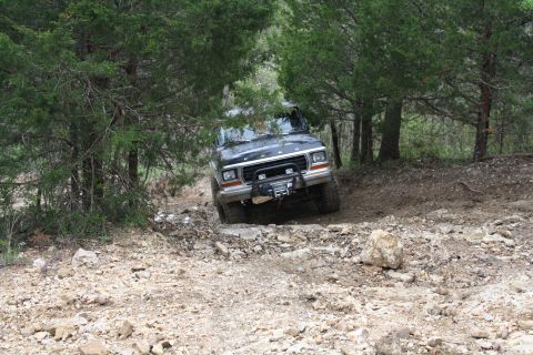 1979 Ford Bronco - This black SUV navigates a challenging rocky trail surrounded by trees.