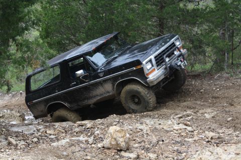 1979 Ford Bronco - A black 1978 Ford Bronco navigates a challenging off-road course, with one wheel deep in mud and rocks.