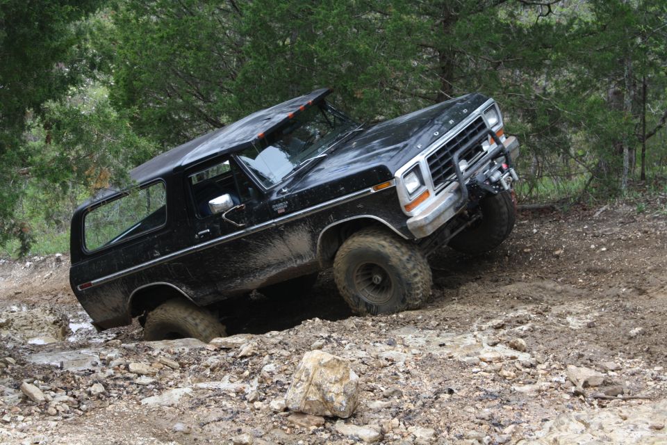Black 1978 Ford Bronco off-roading on a rocky, muddy trail with its front right wheel stuck