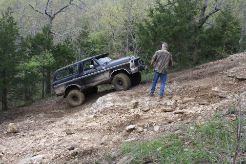 1979 Ford Bronco - A man watches a black Ford Bronco navigate a steep, rocky incline in a wooded area.