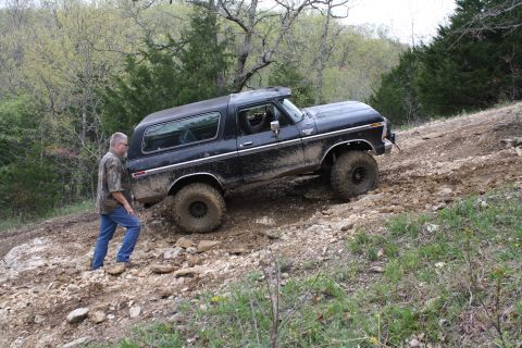 1979 Ford Bronco - A man walks alongside a muddy black 1978 Ford Bronco as it navigates an off-road trail.