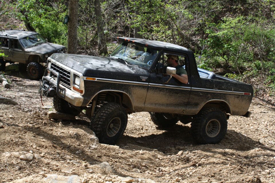Black 1978 Ford Bronco off-roading on a dirt trail, front-left tire elevated