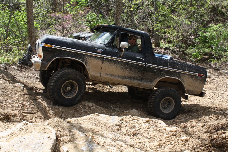 Black Ford Bronco with lifted suspension and large tires driving on a dirt trail