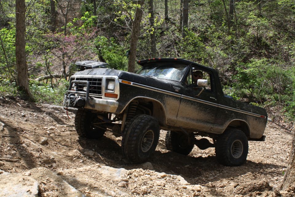 Black 1978 Ford Bronco off-roading on a dirt trail, covered in mud, with a winch on the front bumper