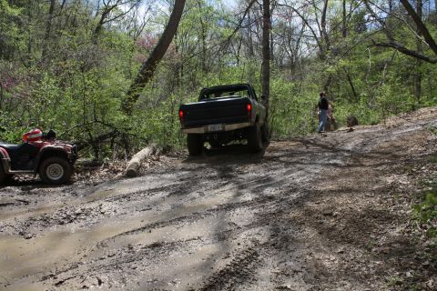 1979 Ford Bronco - A black pickup truck navigates a muddy, wooded trail with an ATV nearby.