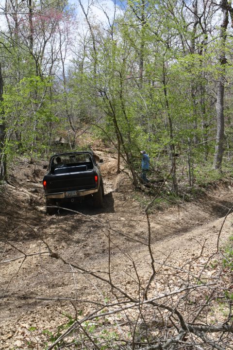 1979 Ford Bronco - A black 1979 Ford Bronco navigates a challenging dirt path through a wooded area.