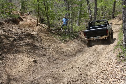 1979 Ford Bronco - A black pickup truck navigates a steep, rutted dirt path in a forest setting.