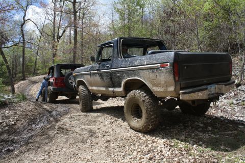 1979 Ford Bronco - Two off-road vehicles navigate a challenging dirt path through a wooded area.