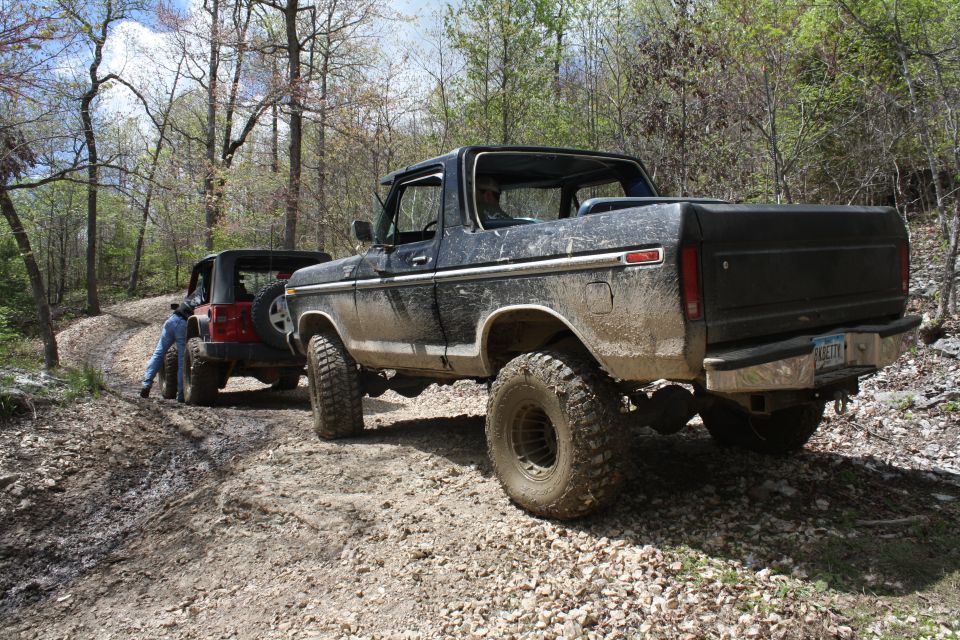 Black 1978 Ford Bronco and red Jeep Wrangler on a muddy off-road trail