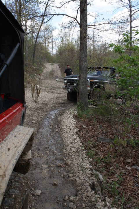 1979 Ford Bronco - Two off-road vehicles navigate a muddy, rocky path through a forest.