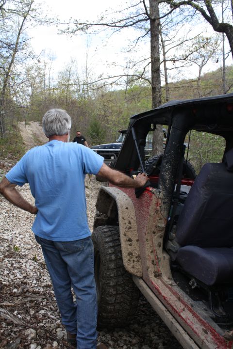 1979 Ford Bronco - Two off-road vehicles are parked on a dirt path surrounded by trees, with one vehicle covered in mud.