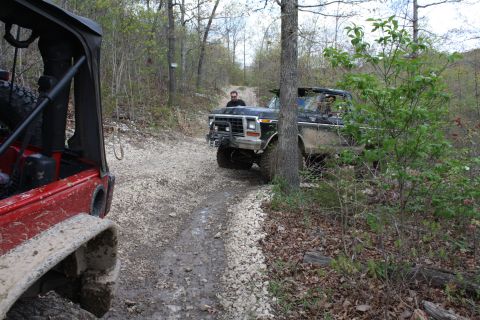 1979 Ford Bronco - A black 1979 Ford Bronco navigates a wooded dirt road, with another vehicle visible in the foreground.