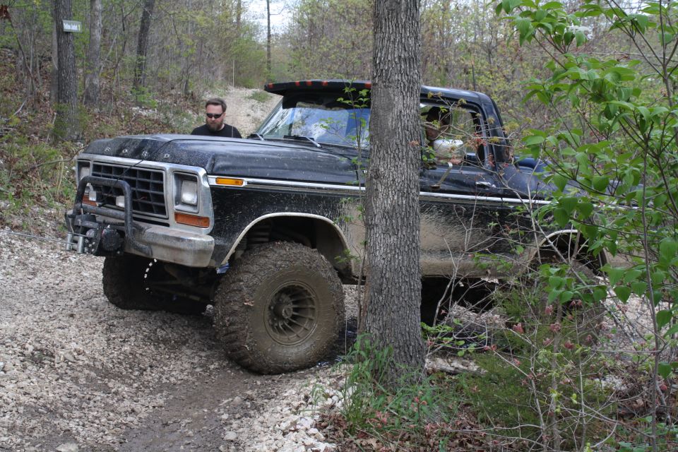 Black 1978 Ford Bronco with large tires on a dirt trail, driver visible