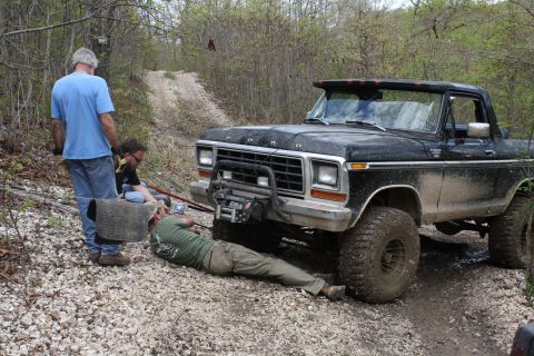 1979 Ford Bronco - A group of people work to free a muddy 1979 Ford Bronco from a difficult spot on a dirt trail.