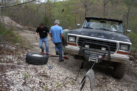 1979 Ford Bronco - Men changing a flat tire on a black Ford Bronco off-road.