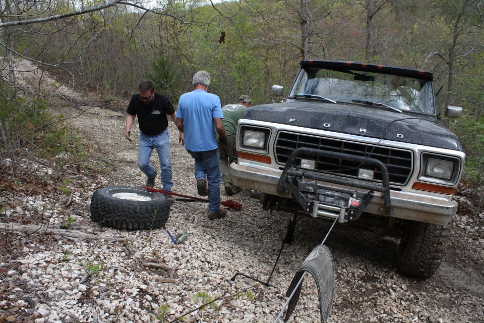 Black Ford Bronco on a dirt road with two men changing a flat tire