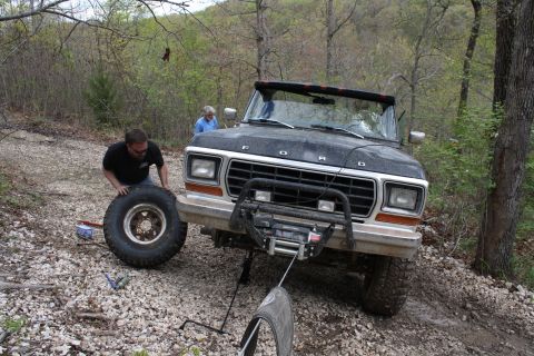 1979 Ford Bronco - A man is preparing to change a tire on a black Ford Bronco, which appears to be stuck on a rocky incline.