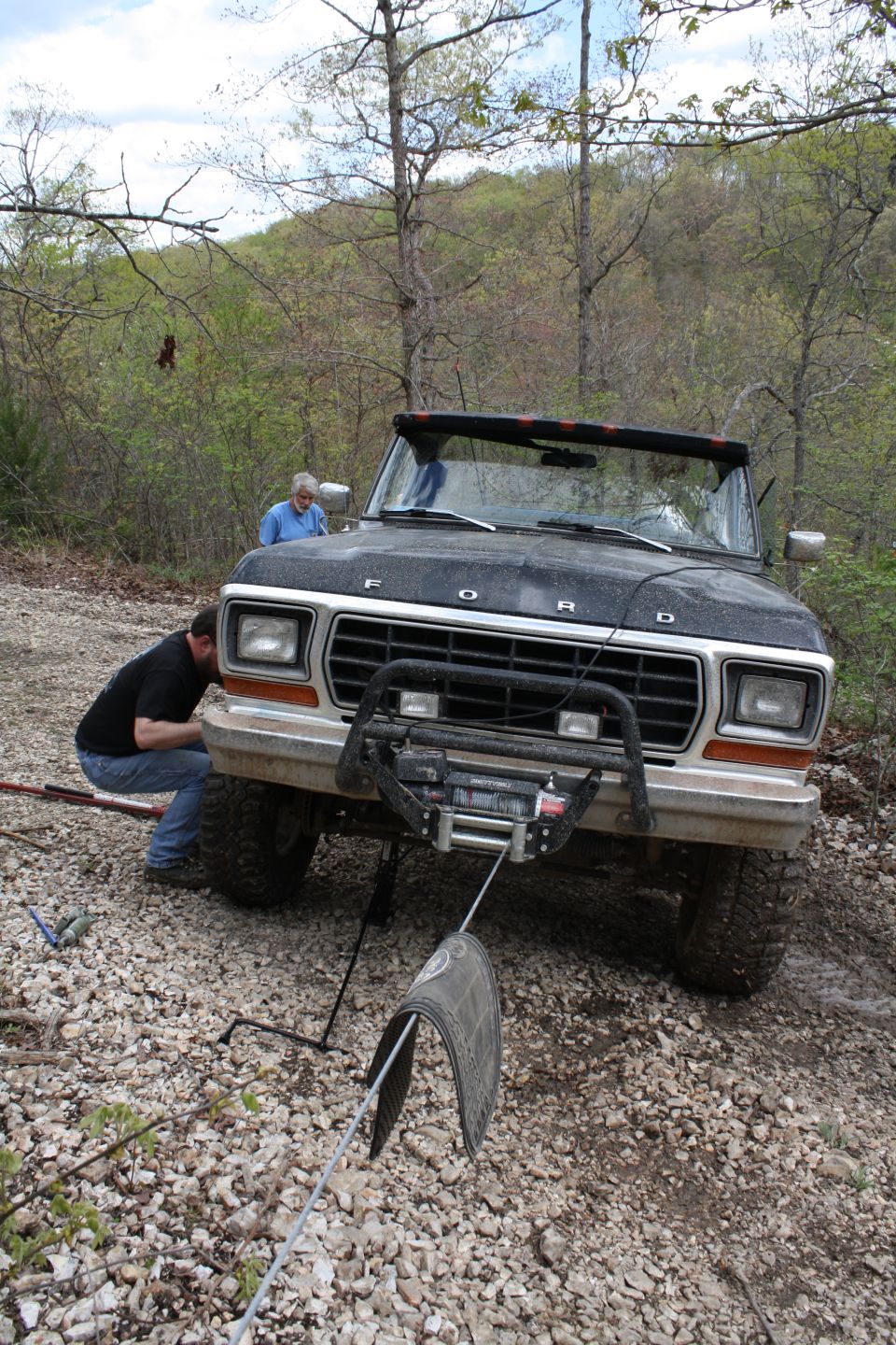 Black 1978 Ford Bronco with a winch and brush guard on a gravel road
