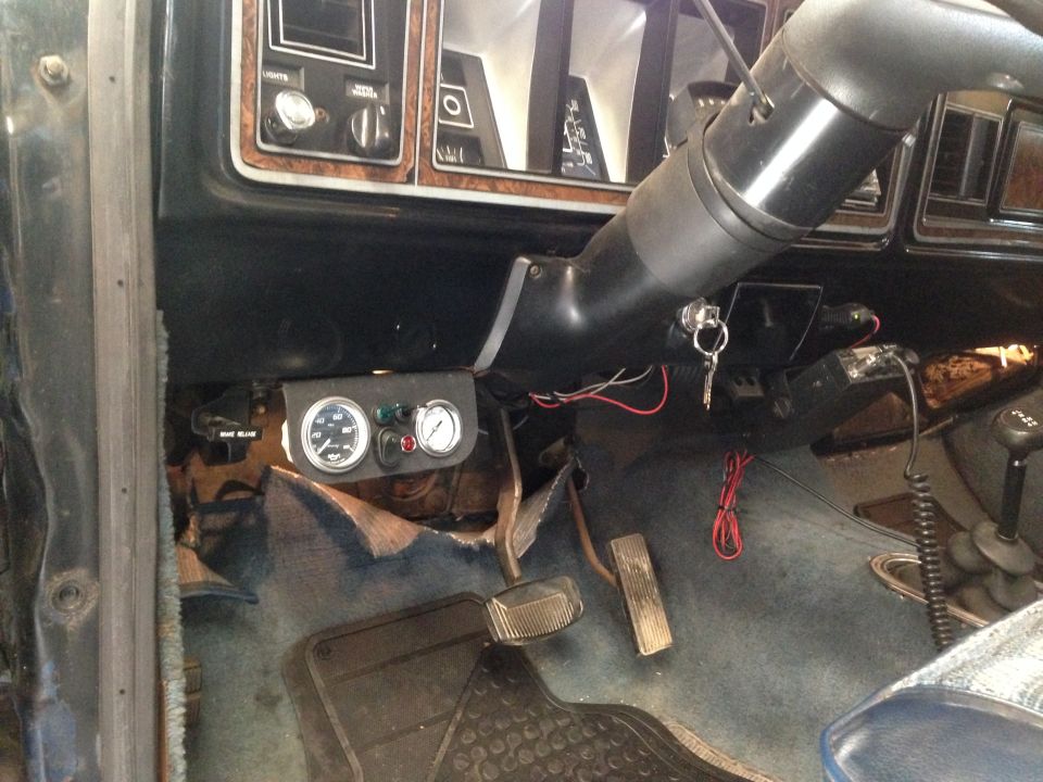 Vehicle interior showing aftermarket gauges mounted below the dashboard, steering column with keys, and floor pedals