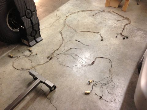 1979 Ford Bronco - A vehicle wiring harness is laid out on a concrete floor, with a tire and jack stand nearby.