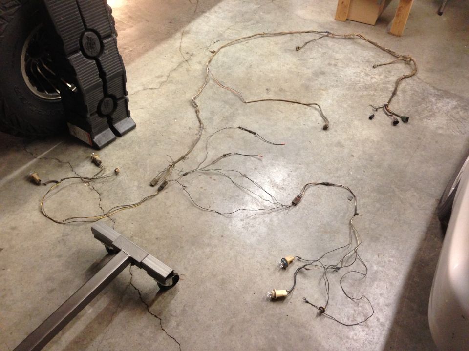 Vehicle wiring harness spread out on concrete floor next to a tire and jack stand