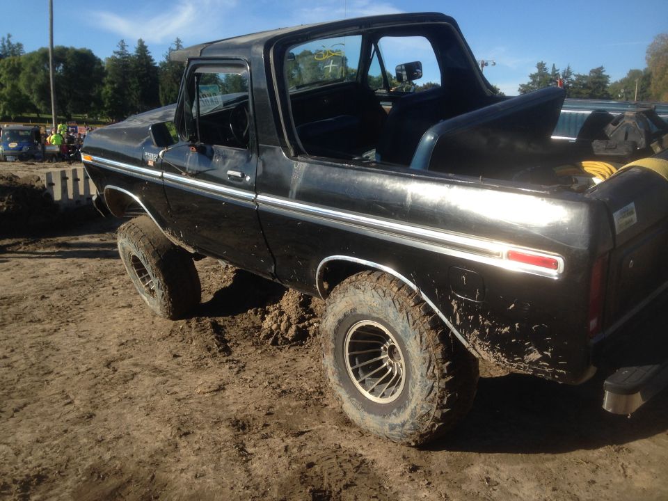 Black SUV with off-road tires stuck in mud, driver's door open