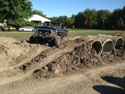 1979 Ford Bronco - A lifted black Ford pickup navigates a dirt obstacle course with concrete pipes and orange flags.