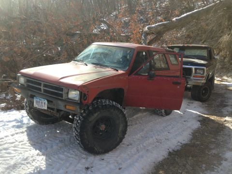 1979 Ford Bronco - Two off-road vehicles, a red Toyota pickup and a black Ford Bronco, are parked in a snowy, wooded landscape.