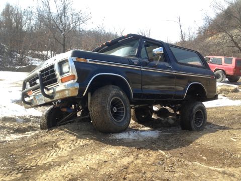 1979 Ford Bronco - Black Ford Bronco navigating an off-road trail with a red SUV in the background.