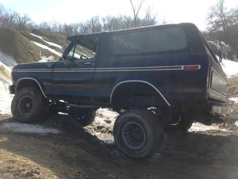 1979 Ford Bronco - This lifted SUV navigates a muddy incline, its dark paint contrasting with the snowy surroundings.