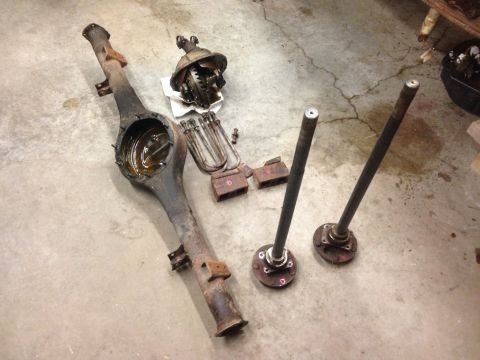 1979 Ford Bronco - Disassembled rear axle components including the housing, differential, and axle shafts are laid out on a concrete surface.