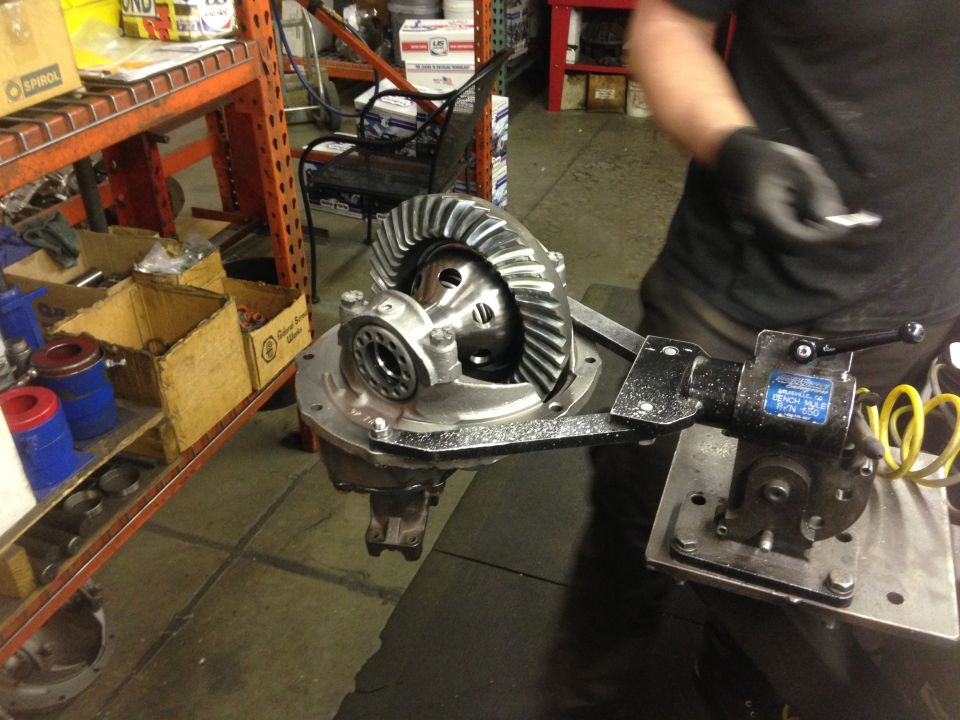 Differential gear assembly mounted in a jig on a workbench, with a person in the background