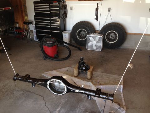 1979 Ford Bronco - A freshly painted rear axle assembly sits on plastic sheeting in a garage, alongside a shop vac and large tires.