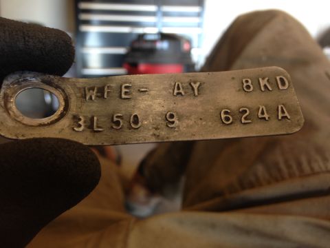 1979 Ford Bronco - A metal tag with stamped codes WFE-AY 8KD 3L50 9 624A is held by a gloved hand.
