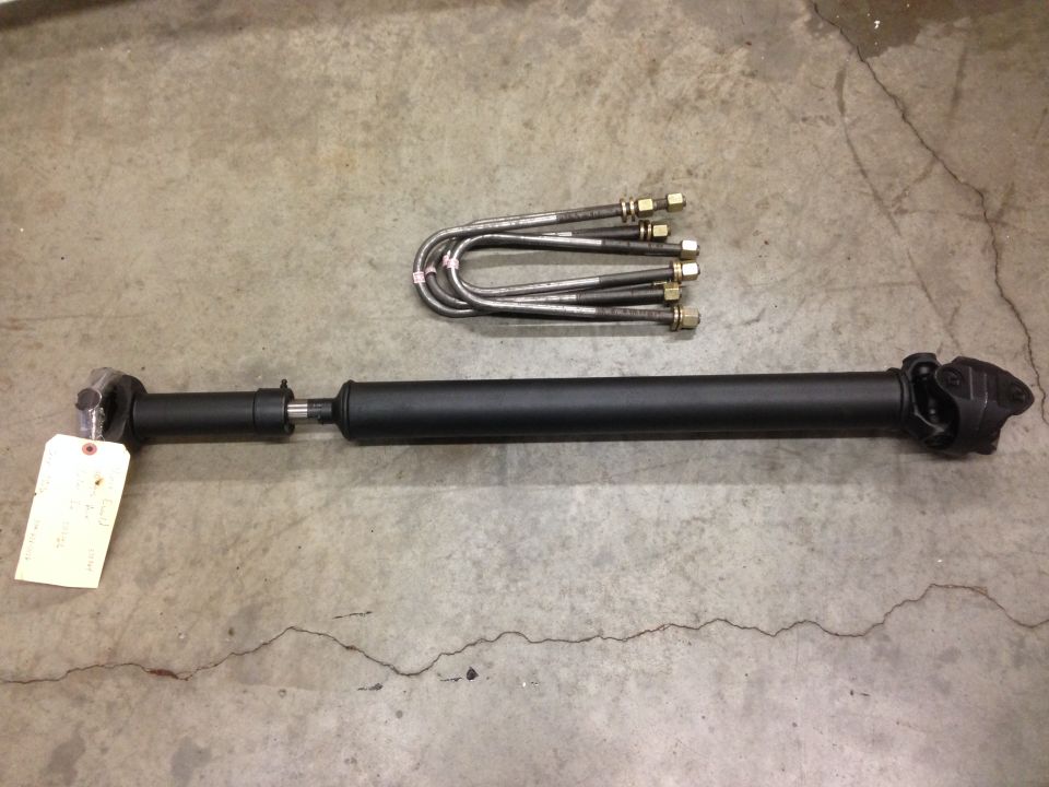 Driveshaft and U-bolts on concrete floor. Driveshaft is black with a tag on the yoke