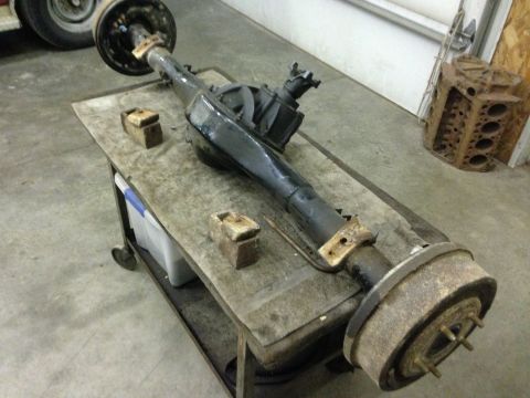 1979 Ford Bronco - A disassembled rear axle assembly rests on a utility cart, with a rusty engine block visible in the background.